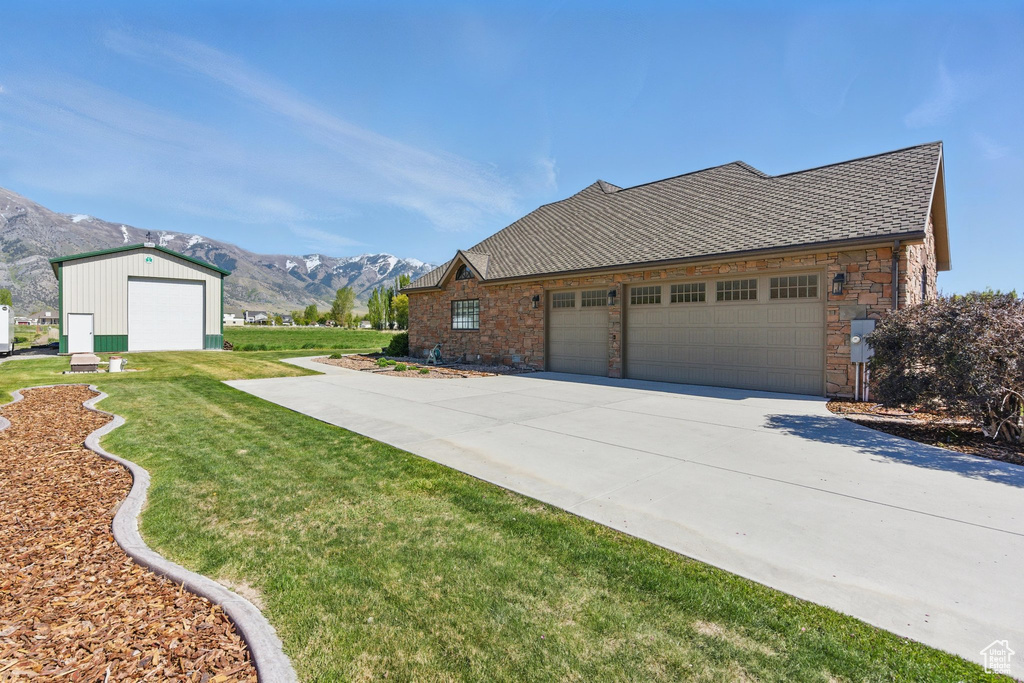 View of side of home featuring an attached garage, stone siding, a mountain view, a yard, and concrete driveway