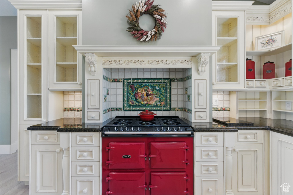 Kitchen featuring glass insert cabinets, light wood finished floors, dark stone countertops, stovetop with downdraft, and tasteful backsplash