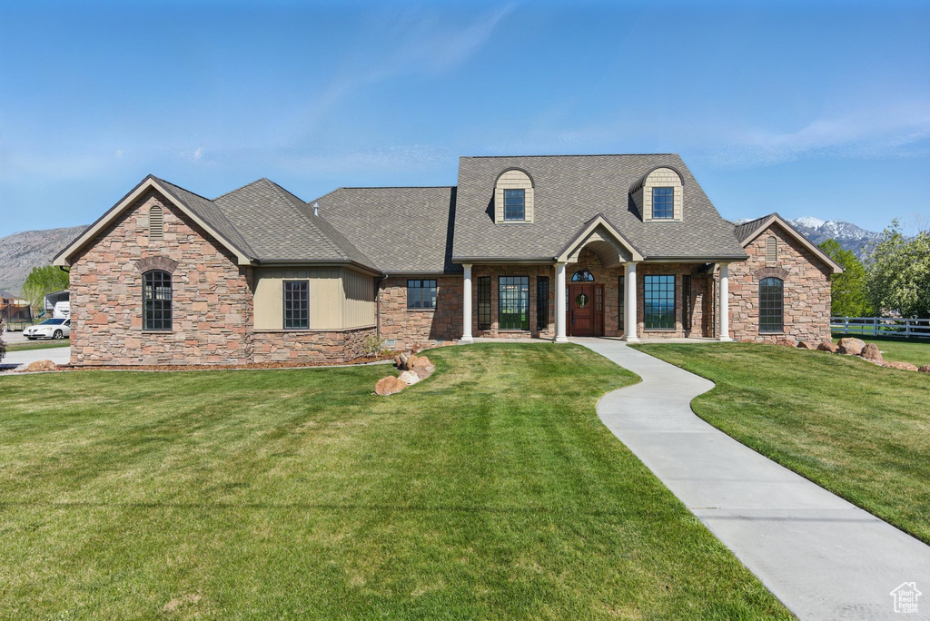 View of front of property featuring stone siding, roof with shingles, a mountain view, and a front yard