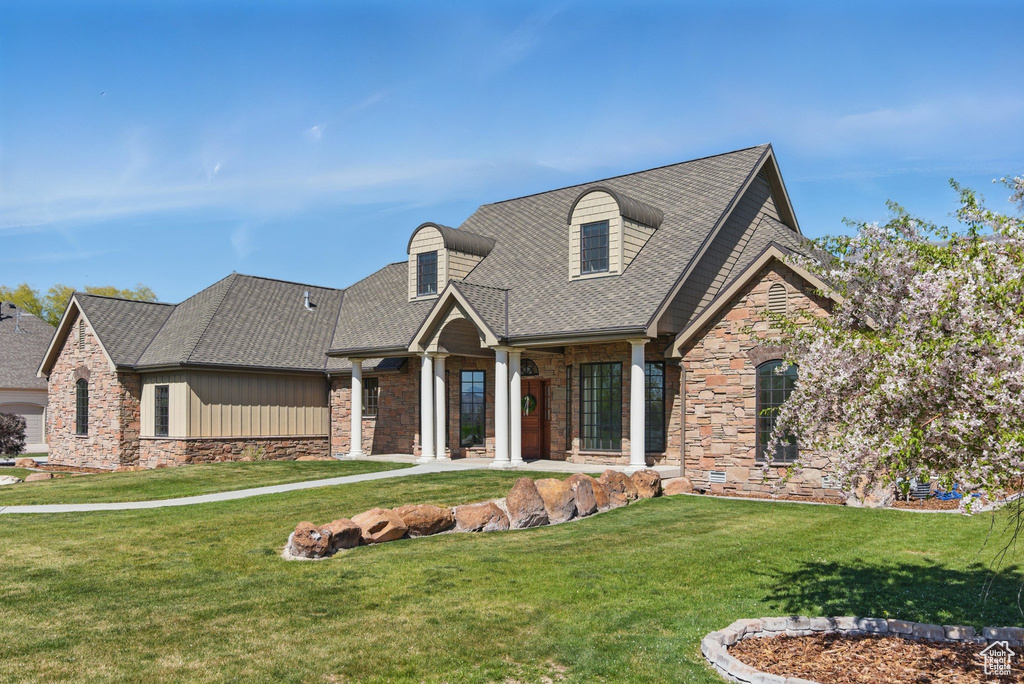 View of front of property featuring roof with shingles, stone siding, and a front yard