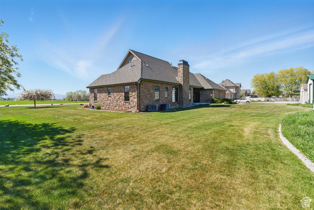 View of side of property with central air condition unit, a chimney, and a lawn