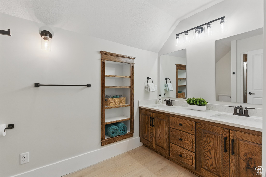 Full bath with vaulted ceiling, double vanity, a sink, and wood finished floors