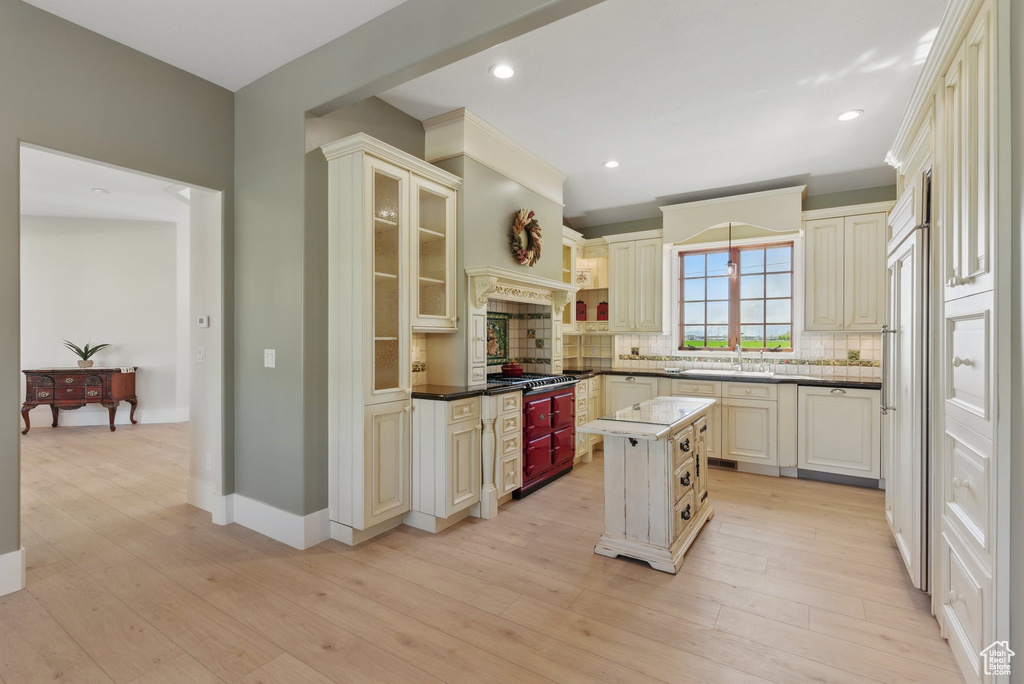 Kitchen featuring stainless steel gas stovetop, a center island, decorative backsplash, light wood-type flooring, and cream cabinets