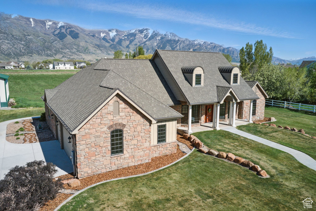 View of front facade with stone siding, a mountain view, fence, and a front lawn