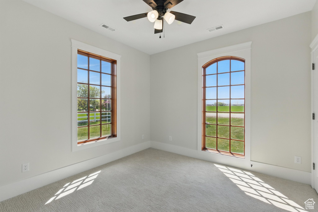 Carpeted empty room featuring a ceiling fan, plenty of natural light, and visible vents