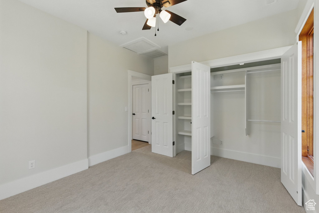 Unfurnished bedroom with a closet, light colored carpet, attic access, a ceiling fan, and baseboards