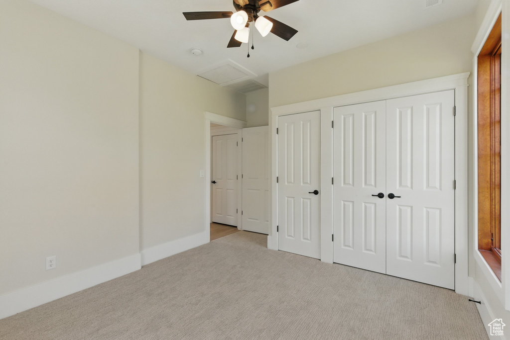 Unfurnished bedroom with two closets, attic access, light colored carpet, and a ceiling fan