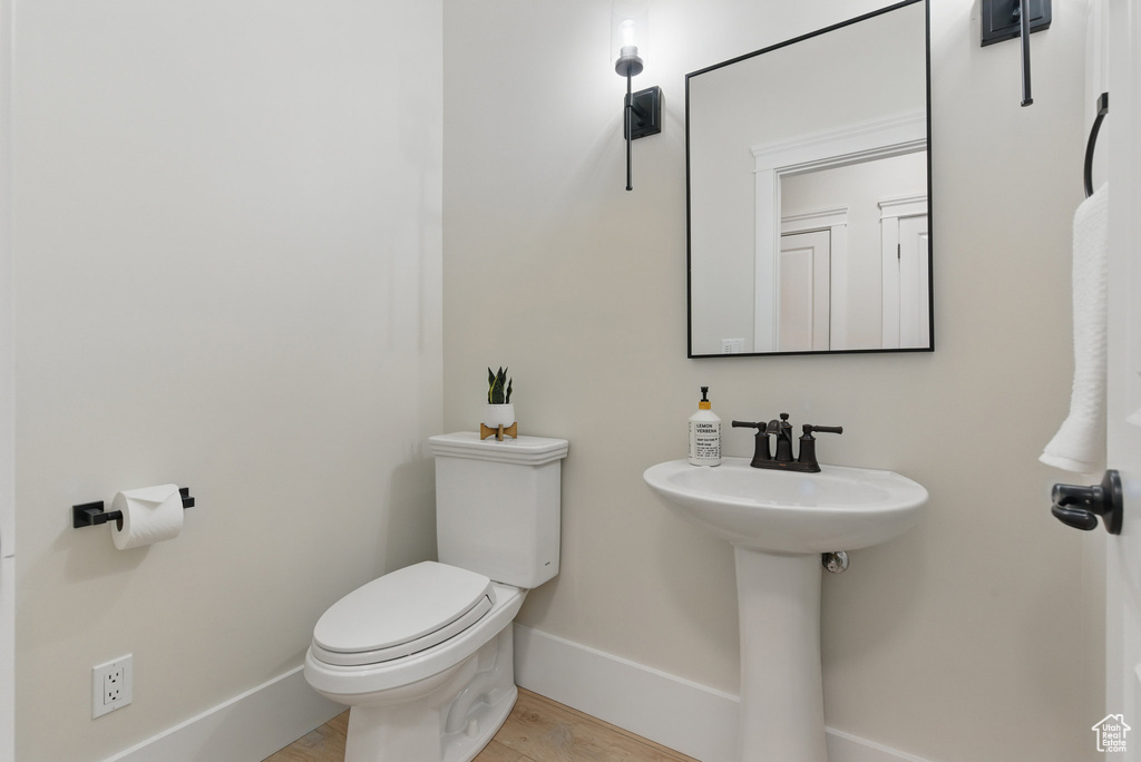 Bathroom featuring toilet, baseboards, wood finished floors, and a sink