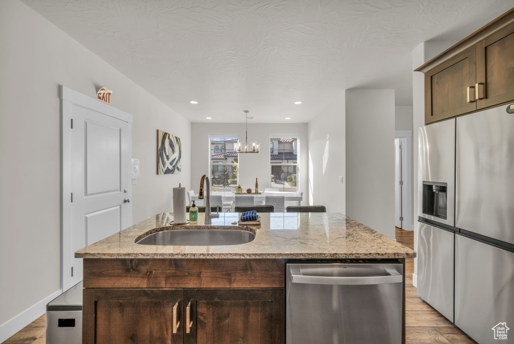 Kitchen featuring stainless steel appliances, a sink, light wood-style flooring, dark brown cabinets, and a center island with sink