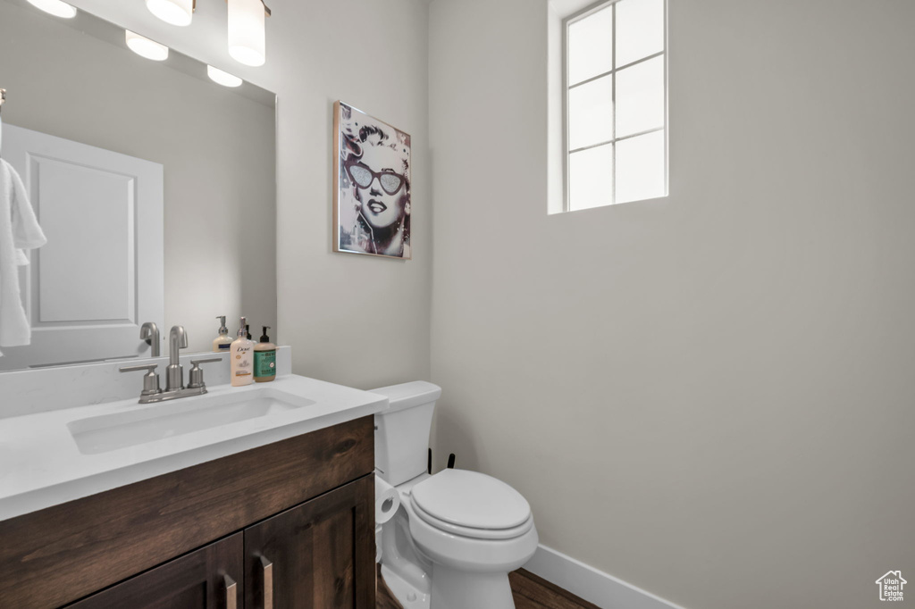 Half bath featuring toilet, vanity, baseboards, and wood finished floors