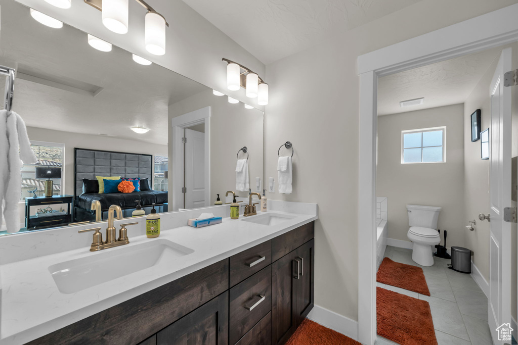 Ensuite bathroom featuring double vanity, baseboards, toilet, a tub, and tile patterned floors