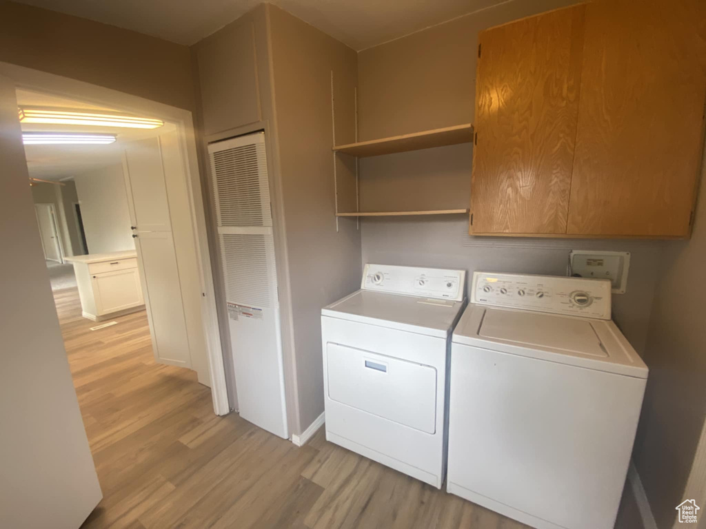 Laundry area featuring independent washer and dryer, light wood-style floors, cabinet space, and baseboards