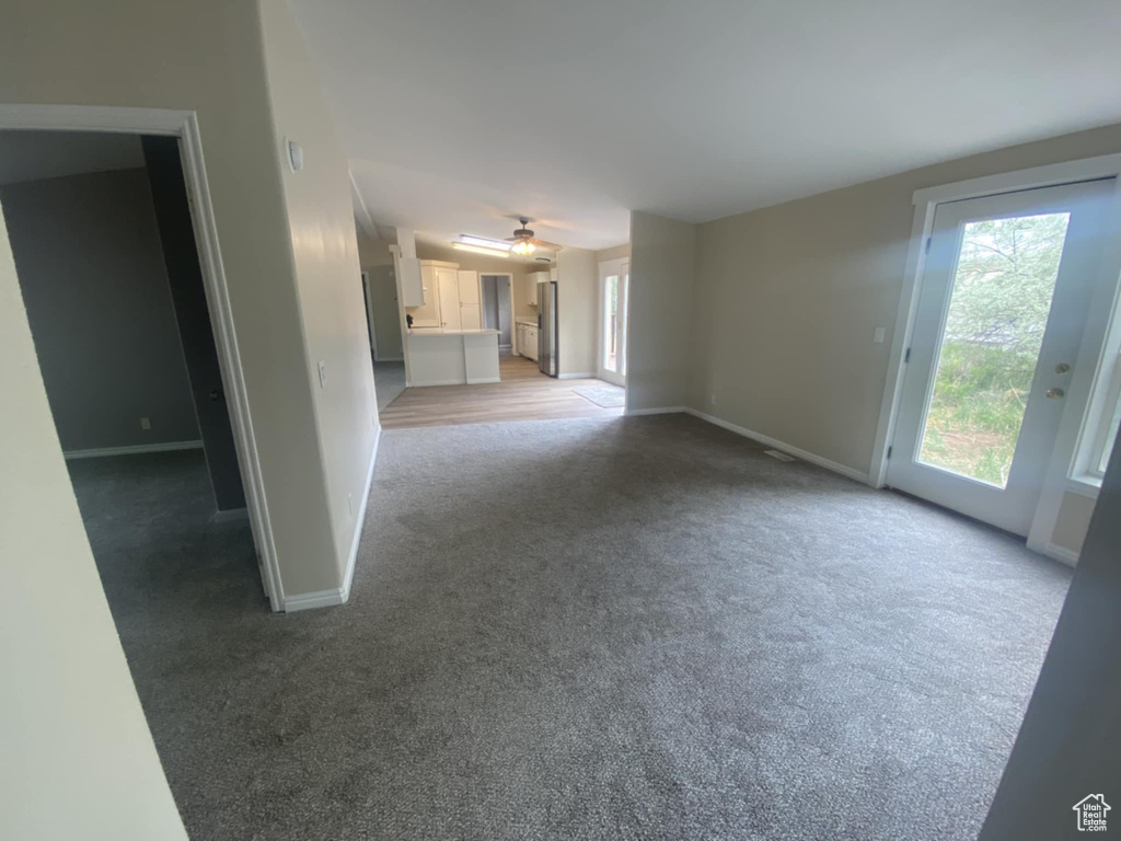 Unfurnished living room with light carpet, baseboards, and a ceiling fan