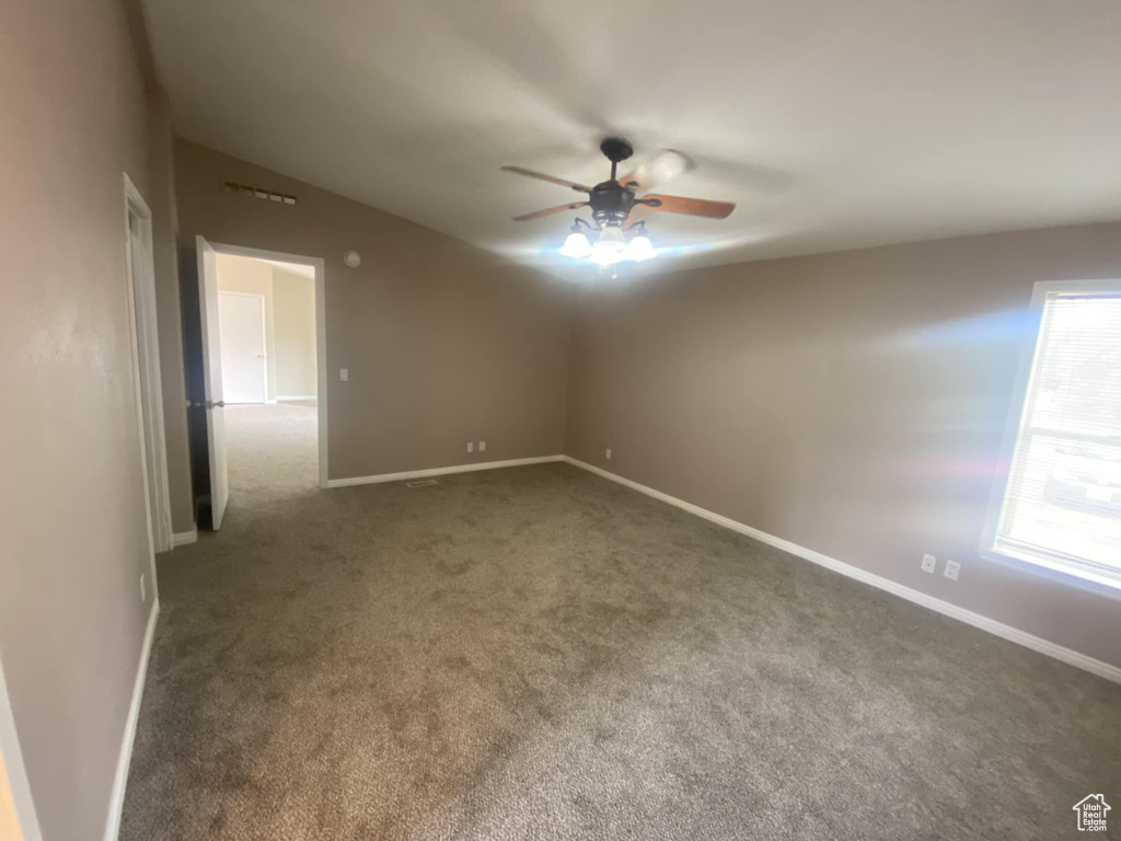 Empty room featuring a ceiling fan, carpet flooring, baseboards, and vaulted ceiling