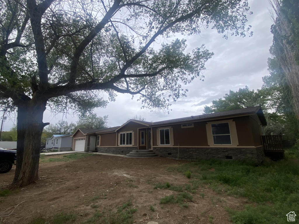 Ranch-style house featuring an attached garage, dirt driveway, stone siding, and crawl space