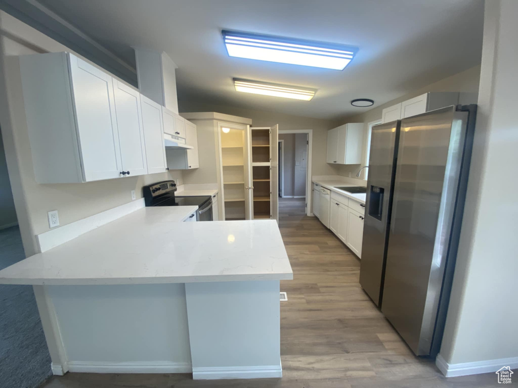 Kitchen featuring appliances with stainless steel finishes, a sink, a peninsula, white cabinetry, and under cabinet range hood