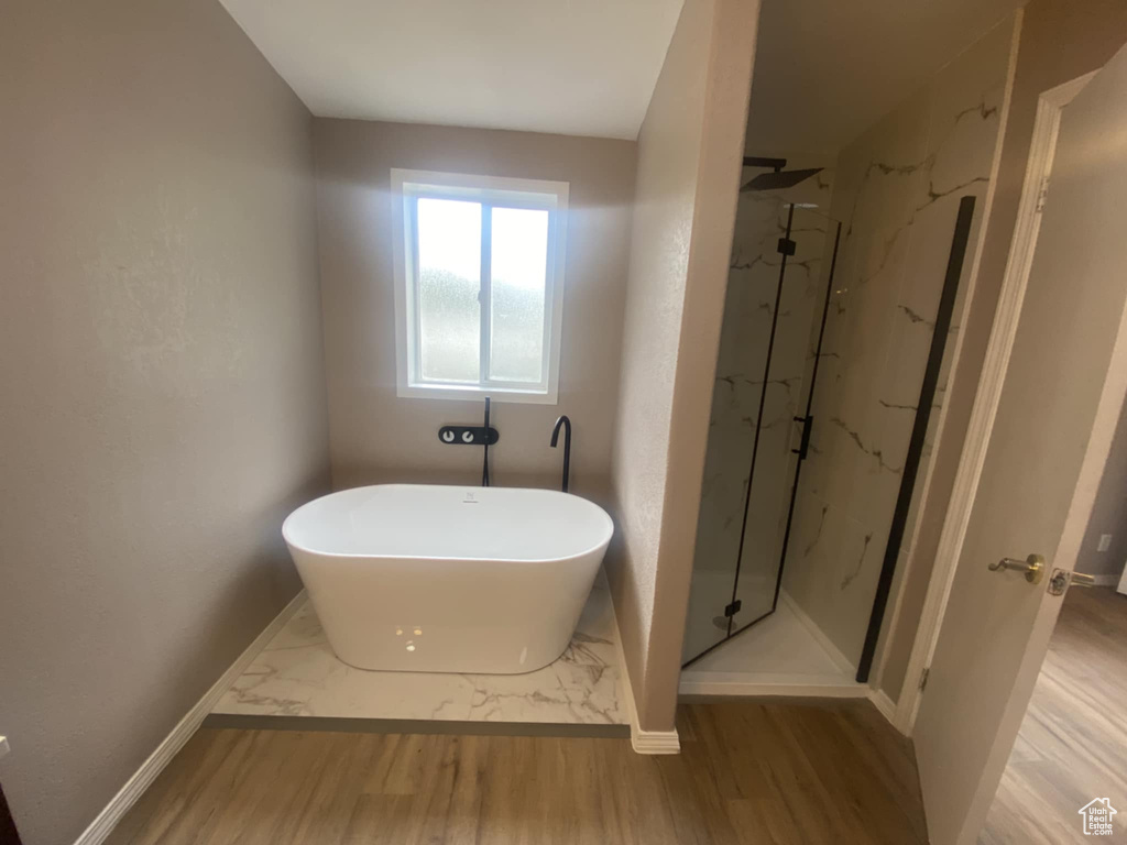 Full bath featuring a marble finish shower, a freestanding tub, wood finished floors, and baseboards