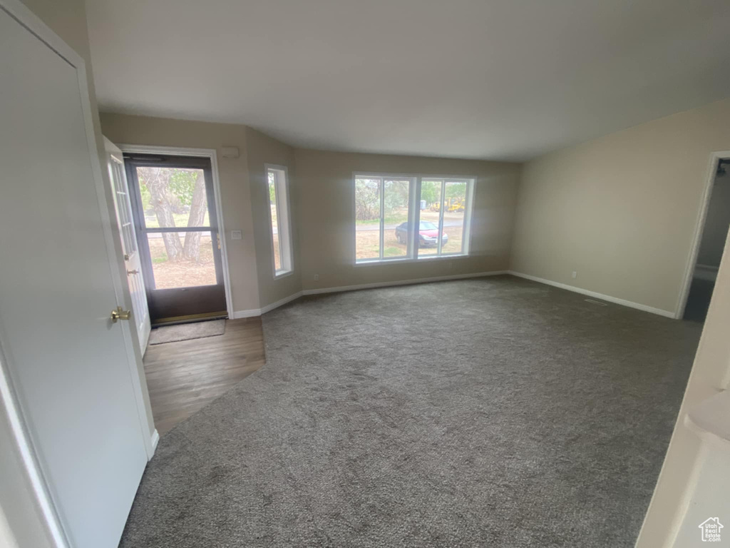 Unfurnished living room with carpet floors, plenty of natural light, and baseboards