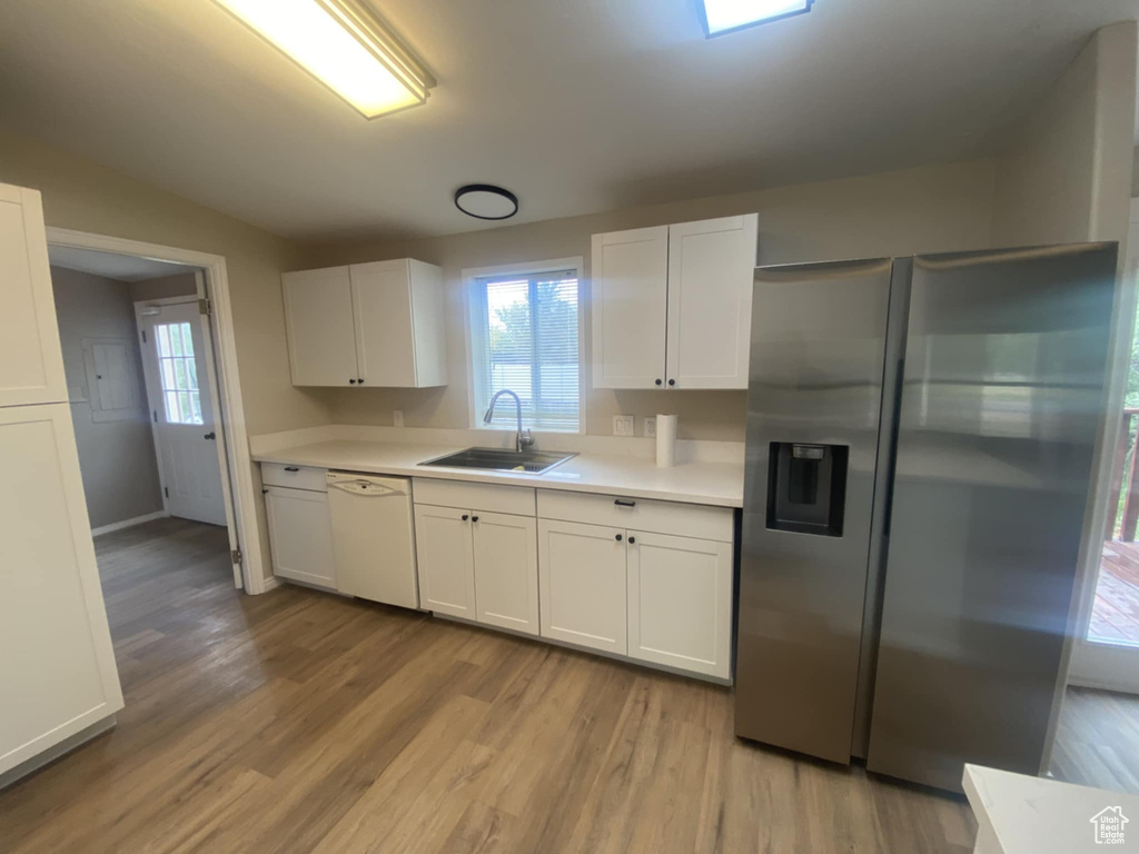 Kitchen with a sink, stainless steel refrigerator with ice dispenser, white dishwasher, light countertops, and light wood-type flooring