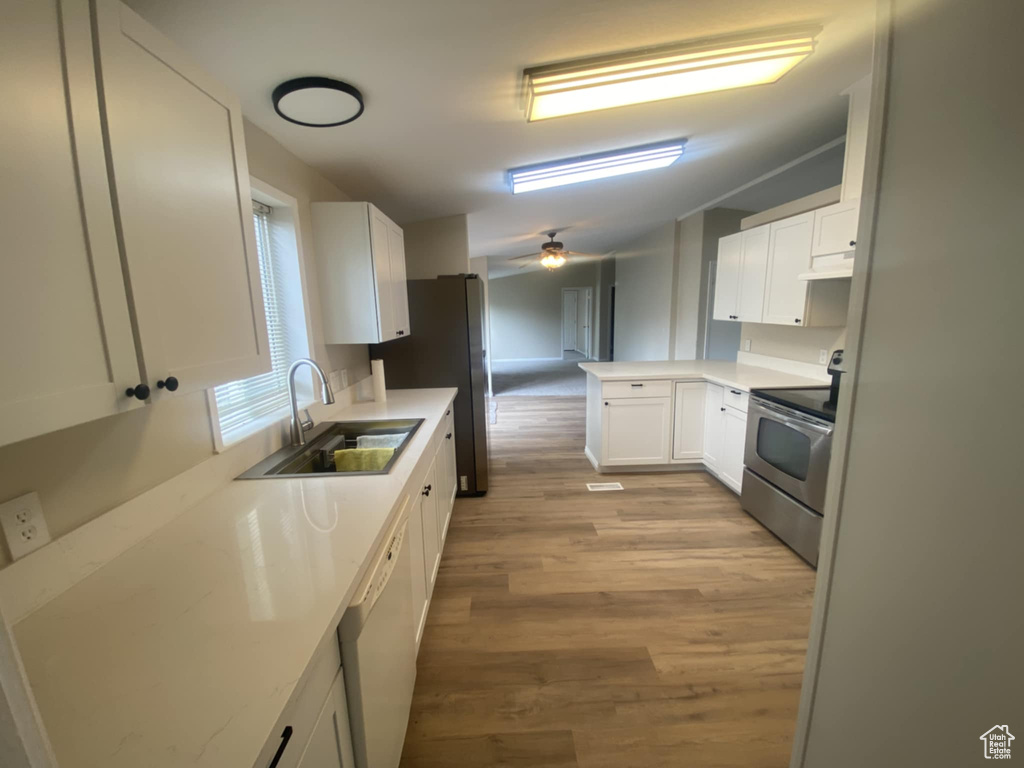 Kitchen with appliances with stainless steel finishes, a sink, light wood-type flooring, white cabinetry, and under cabinet range hood