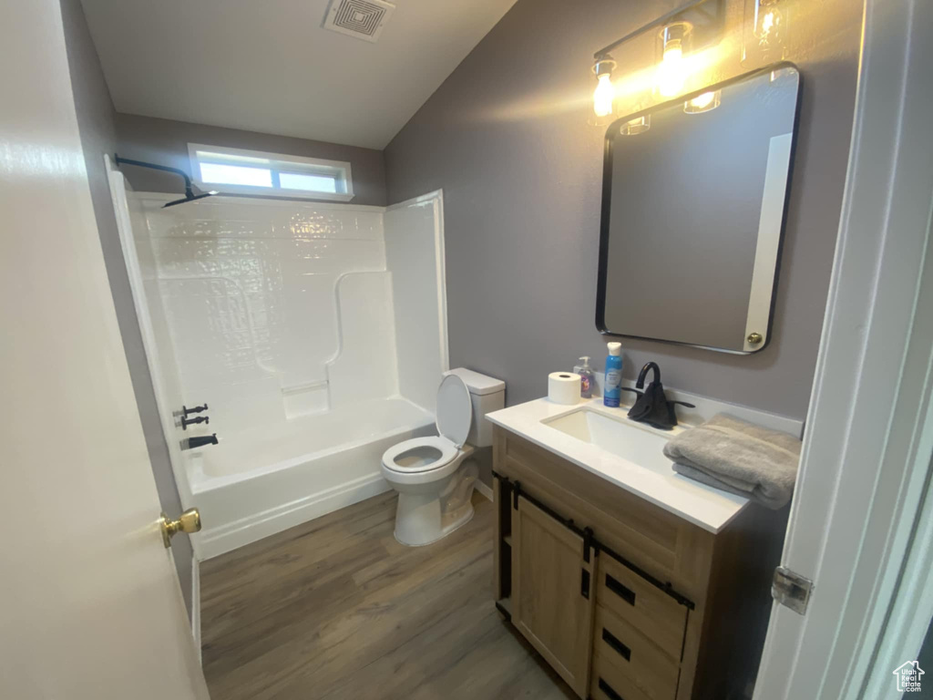 Full bath with toilet, wood finished floors, vaulted ceiling, vanity, and shower / tub combination