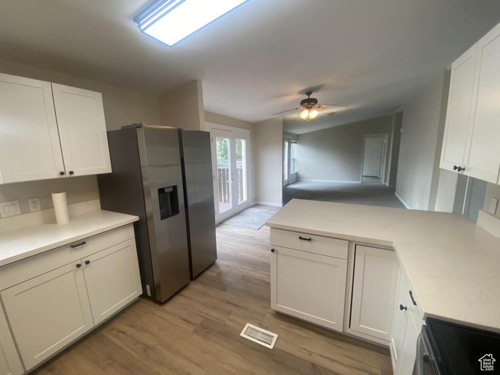 Kitchen featuring stainless steel appliances, a peninsula, white cabinets, light countertops, and light wood-type flooring