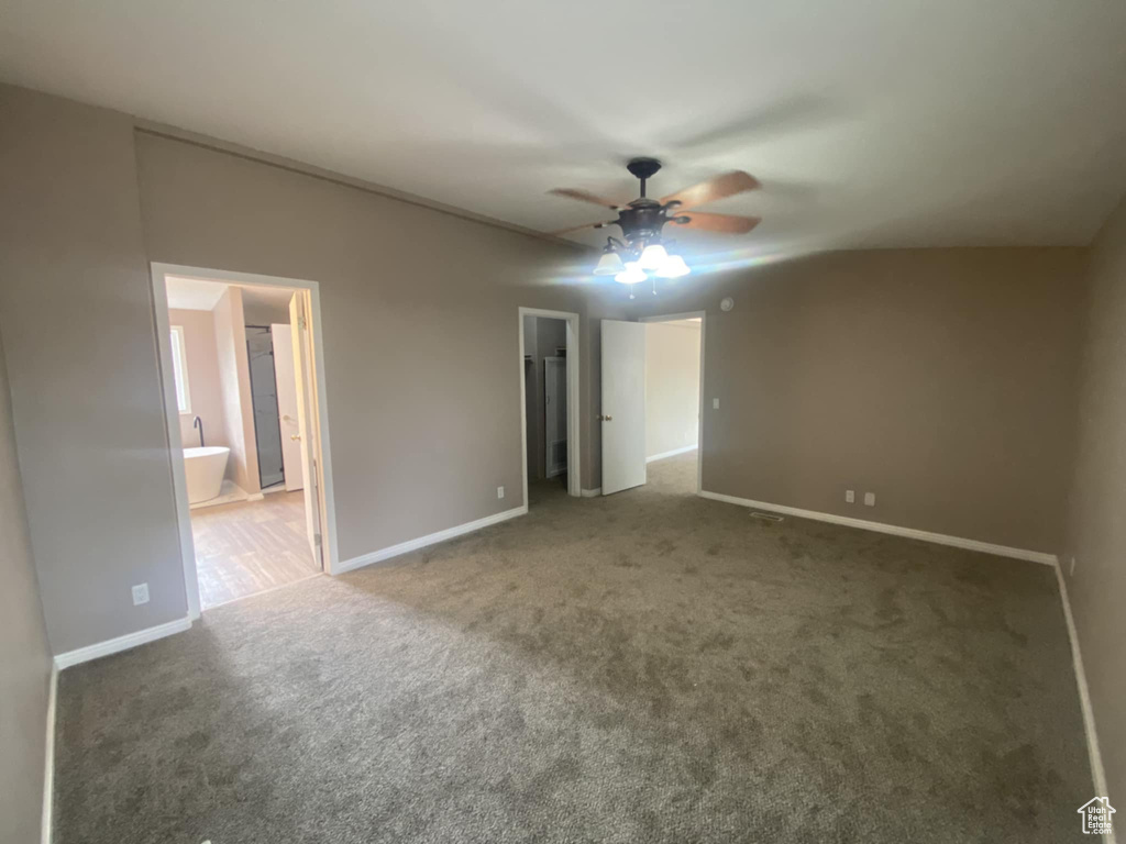 Unfurnished bedroom featuring a walk in closet, carpet floors, baseboards, ensuite bath, and ceiling fan