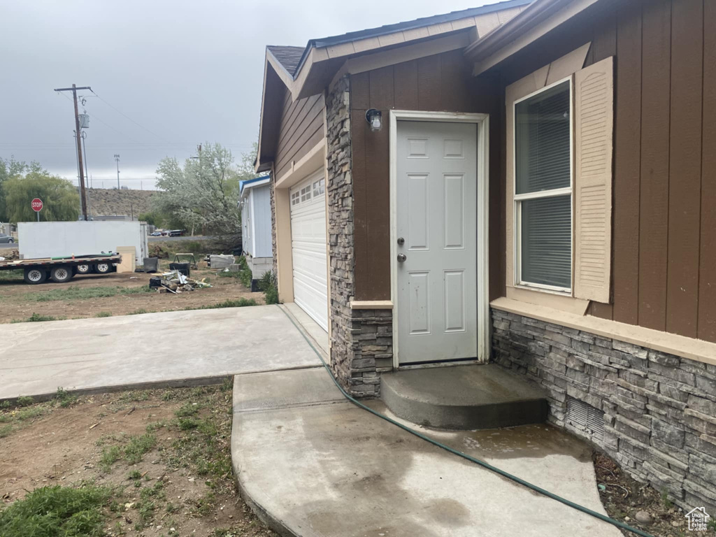 Entrance to property featuring stone siding, a garage, concrete driveway, and board and batten siding