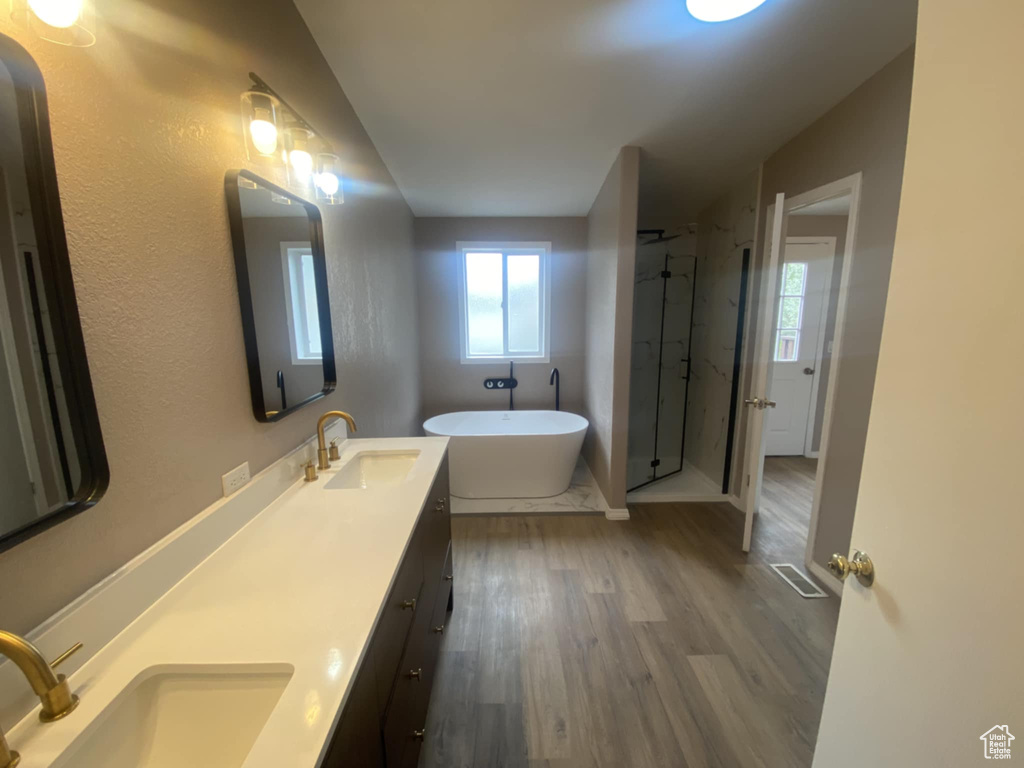 Full bathroom featuring a soaking tub, wood finished floors, a stall shower, and double vanity