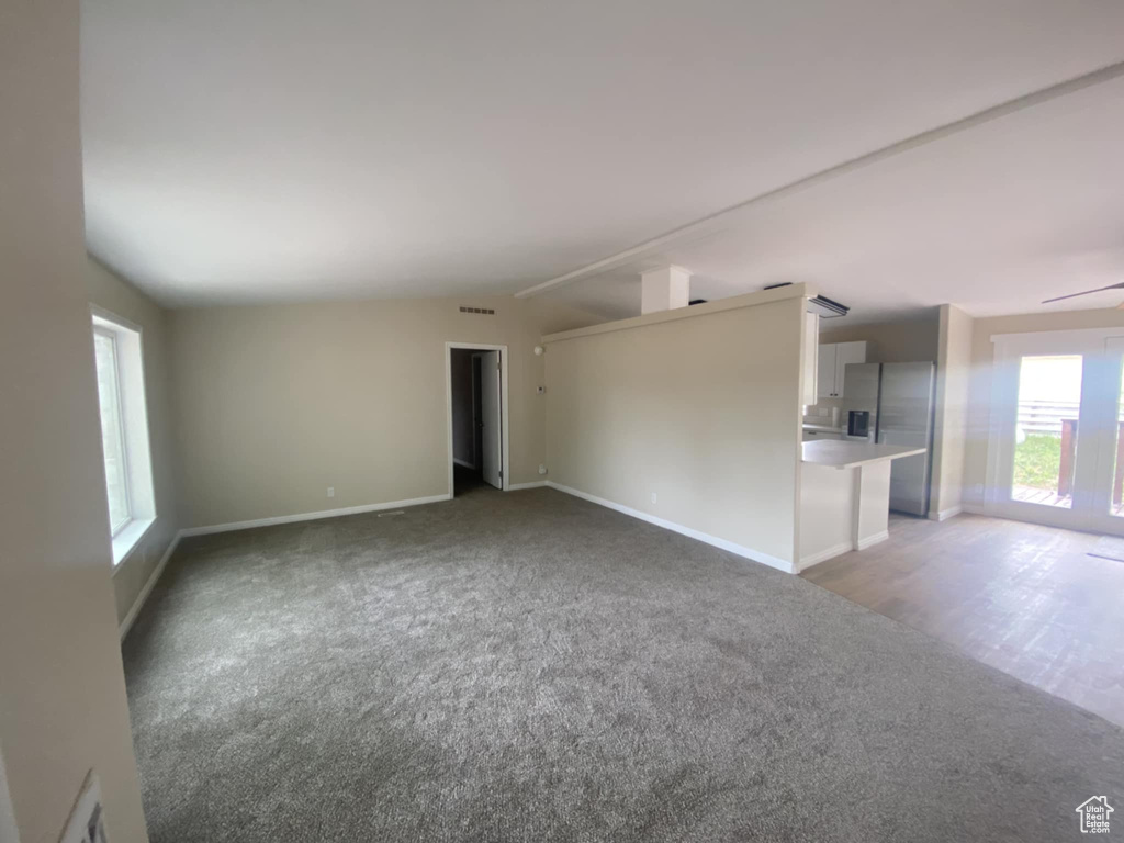 Unfurnished living room featuring light colored carpet, vaulted ceiling, and baseboards