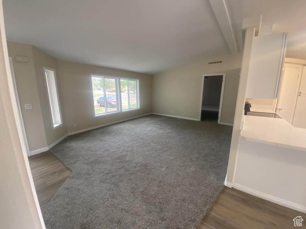 Unfurnished living room with vaulted ceiling, baseboards, wood finished floors, and carpet floors