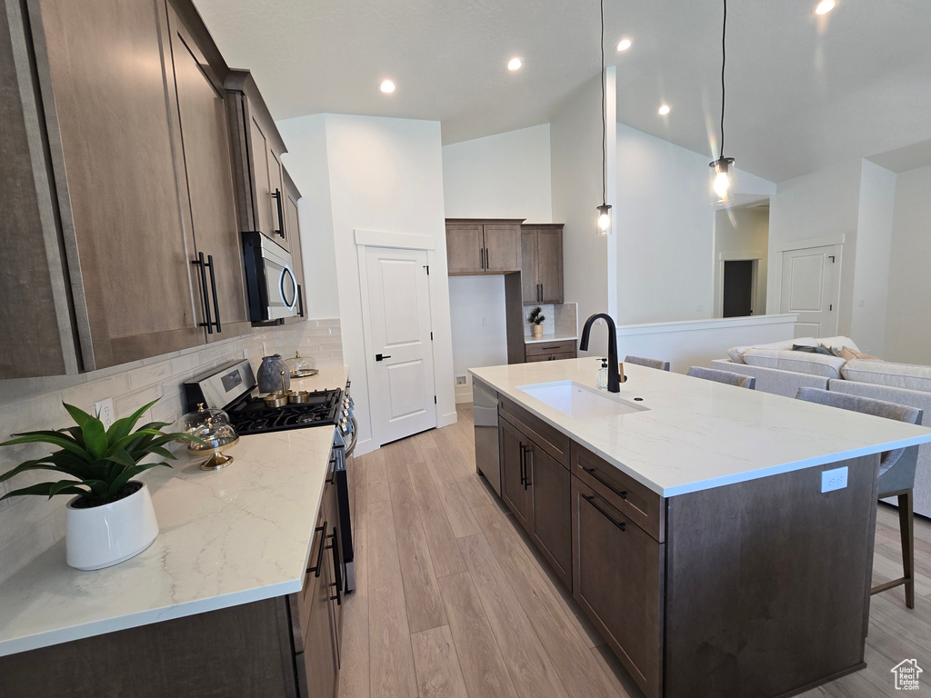 Kitchen featuring stainless steel appliances, a sink, tasteful backsplash, a center island with sink, and light wood-style floors