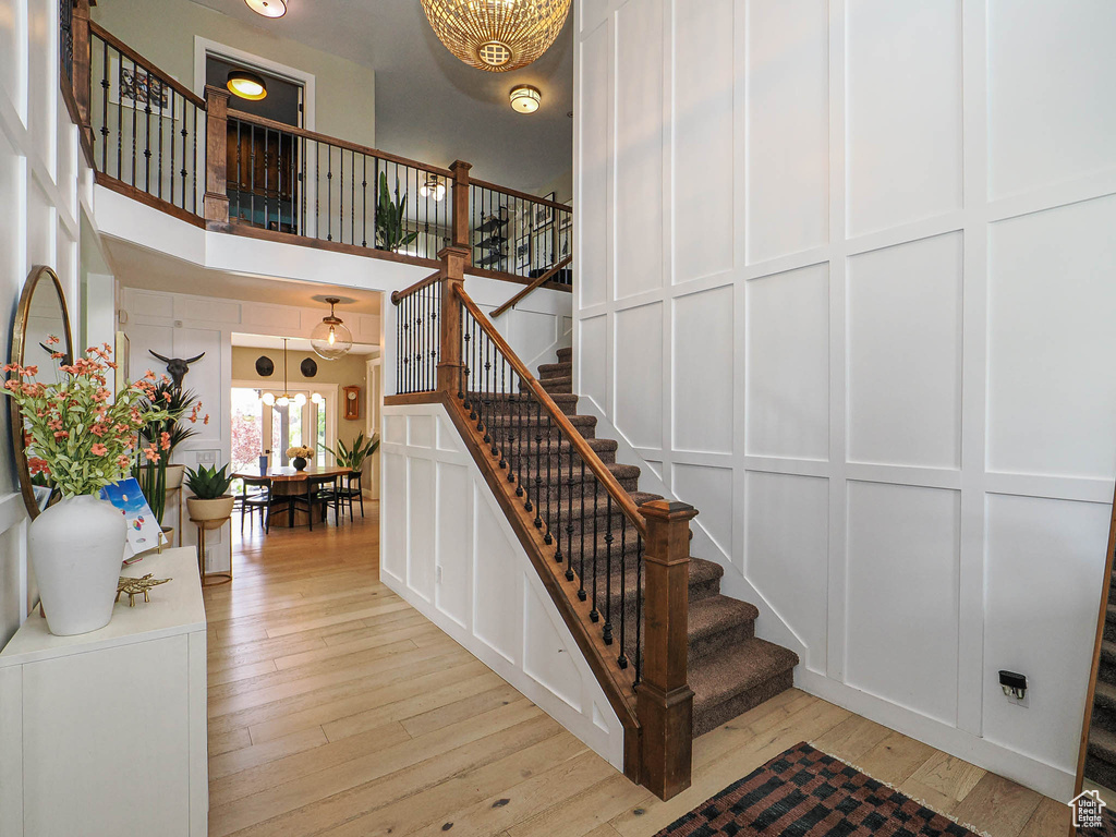 Stairs featuring a chandelier, wood-type flooring, a high ceiling, and a decorative wall