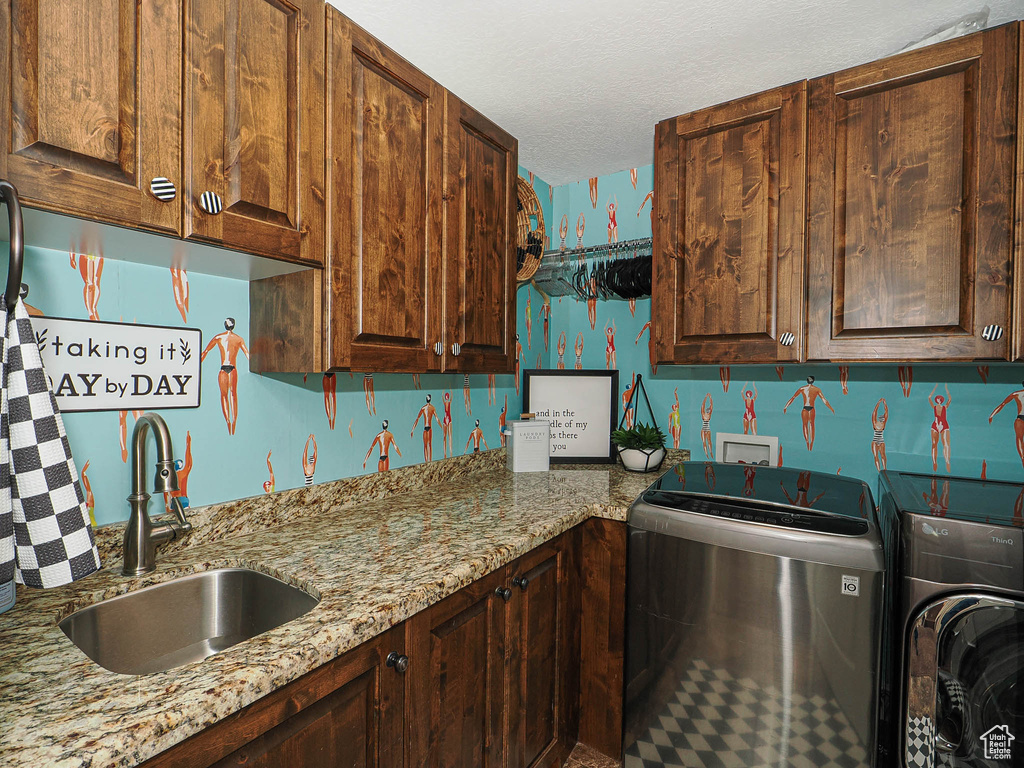 Washroom with washer and clothes dryer, cabinet space, a textured ceiling, and wallpapered walls