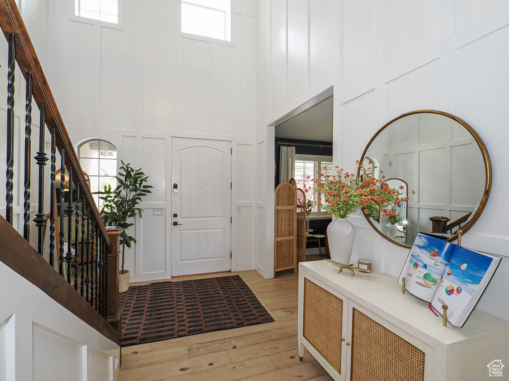 Entrance foyer with a decorative wall, light wood-type flooring, stairs, healthy amount of natural light, and a high ceiling
