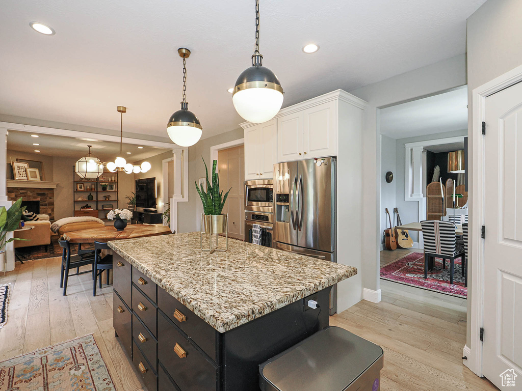 Kitchen with stainless steel appliances, white cabinets, a fireplace, light wood-style flooring, and a kitchen island