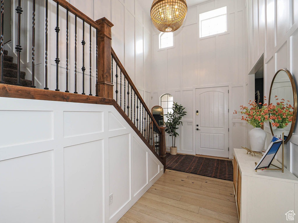 Entryway with a decorative wall, light wood-style flooring, stairway, a chandelier, and a high ceiling