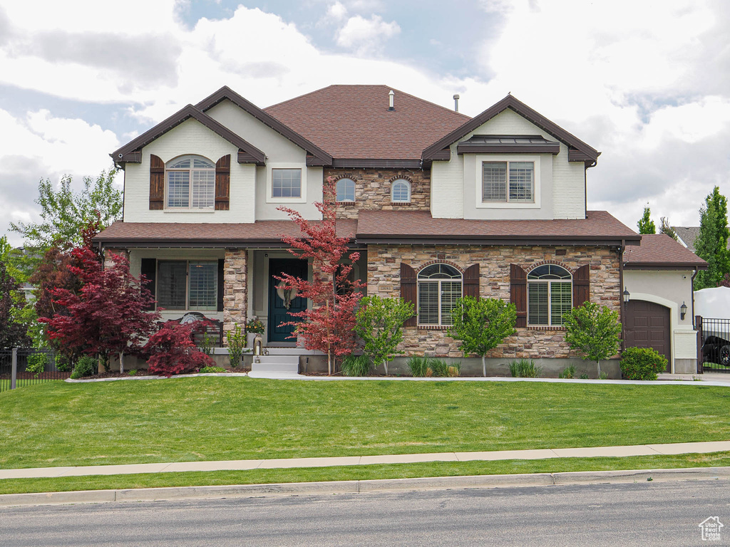 View of front of house with a garage, stone siding, a front lawn, a porch, and roof with shingles