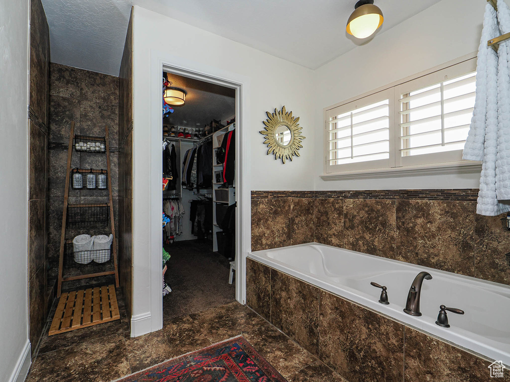 Full bath with a spacious closet, a bath, and tiled shower