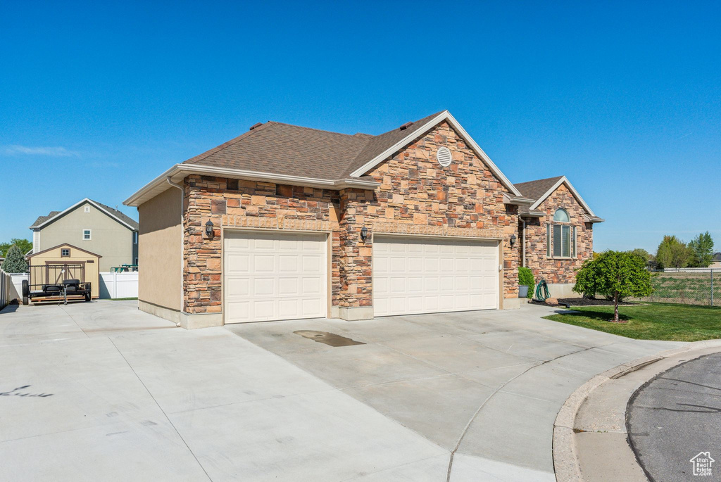 View of front of home featuring concrete driveway, stone siding, a shingled roof, and a garage