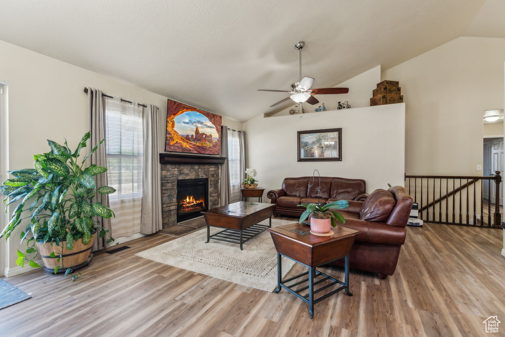 Living area featuring vaulted ceiling, wood finished floors, a fireplace, and a ceiling fan
