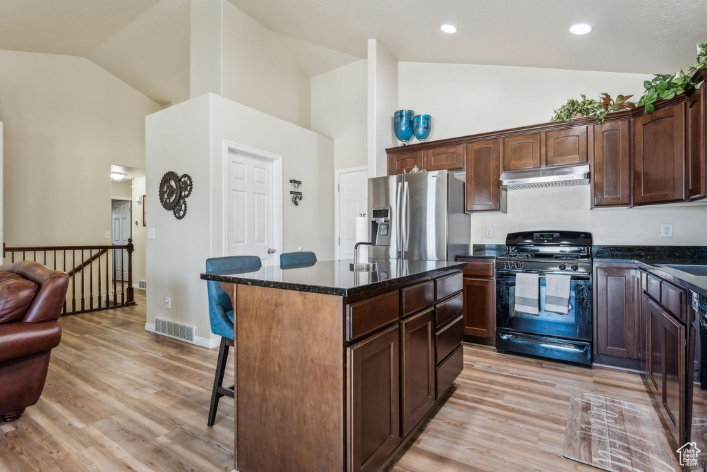 Kitchen featuring black gas range, stainless steel fridge, high vaulted ceiling, under cabinet range hood, and a kitchen breakfast bar