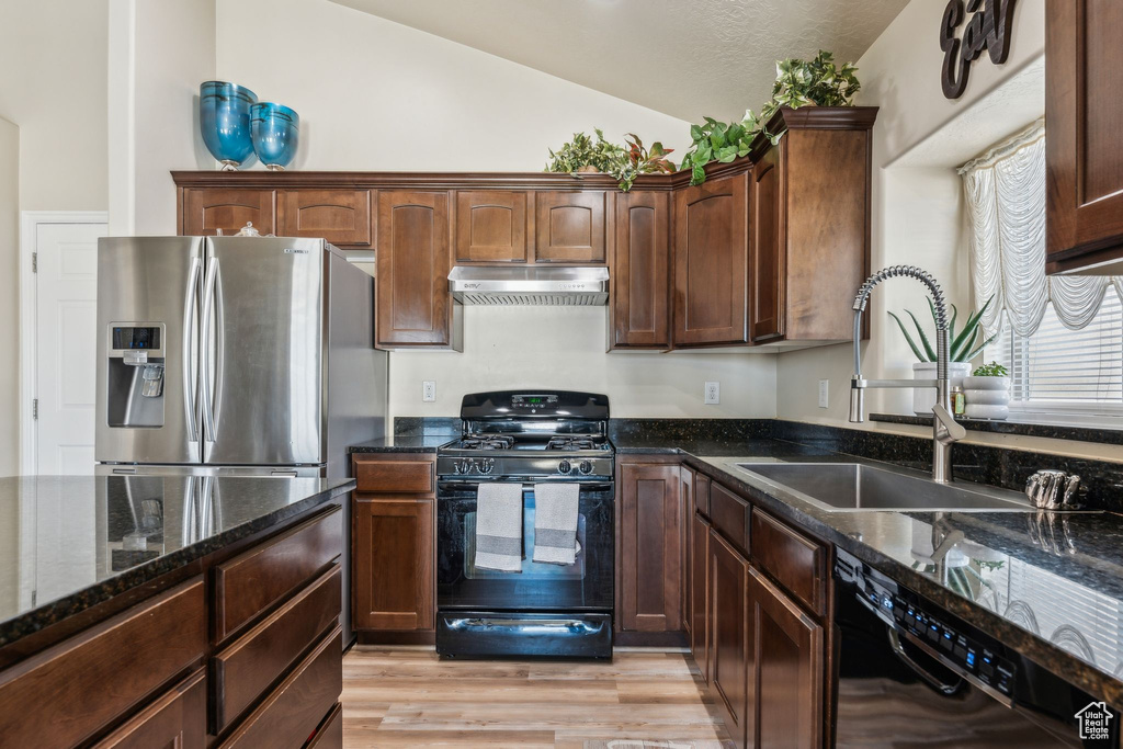 Kitchen with black appliances, under cabinet range hood, lofted ceiling, dark stone countertops, and a sink