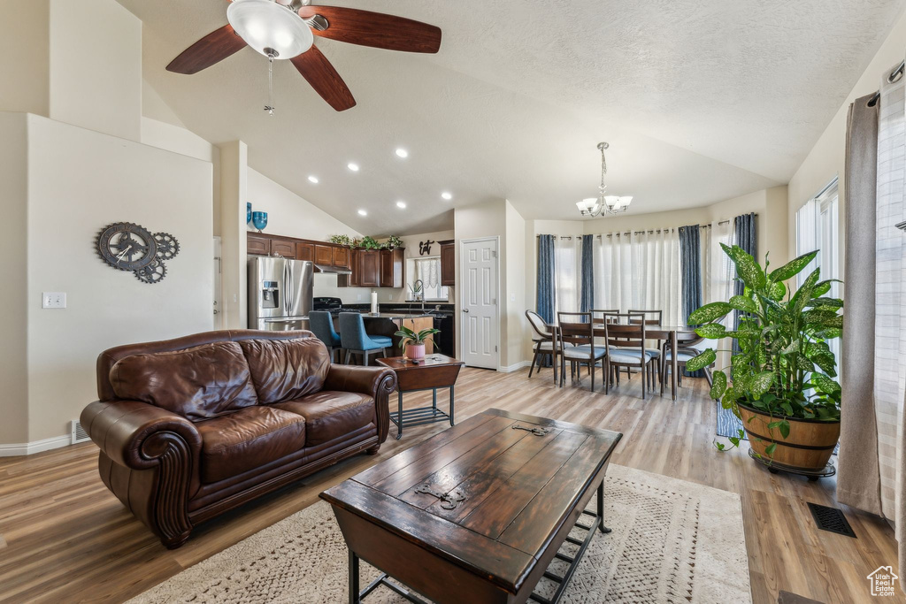 Living room featuring vaulted ceiling, light wood-style flooring, a chandelier, baseboards, and ceiling fan
