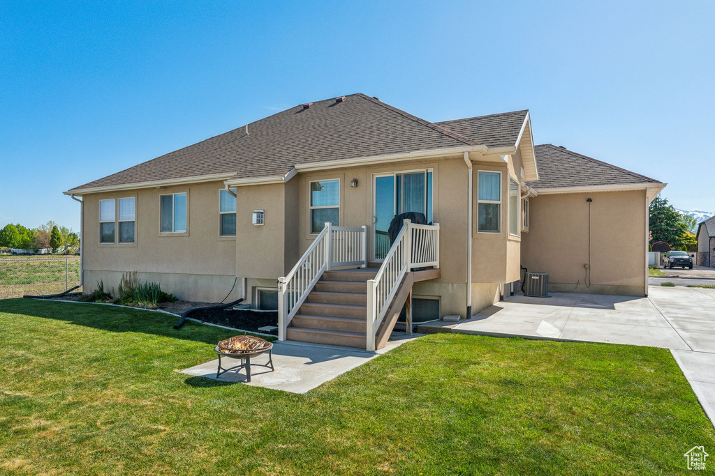 Rear view of house featuring stucco siding, an outdoor fire pit, a patio area, a yard, and central air condition unit