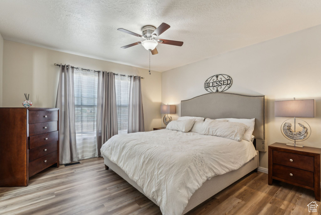 Bedroom with wood finished floors, a textured ceiling, and a ceiling fan