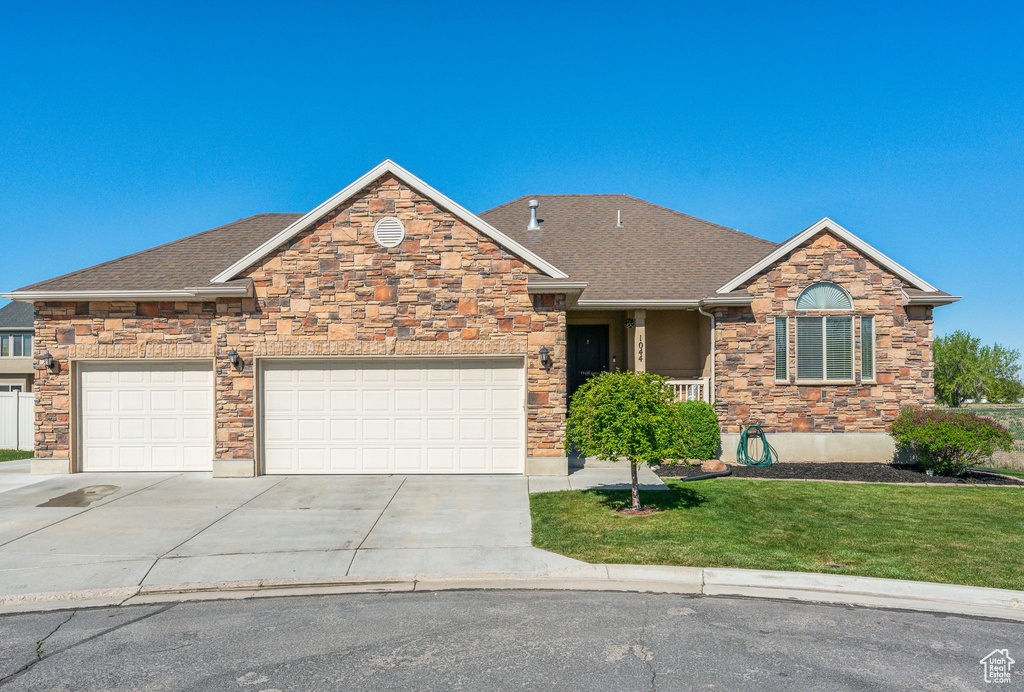 View of front of property featuring concrete driveway, a front lawn, an attached garage, roof with shingles, and stone siding