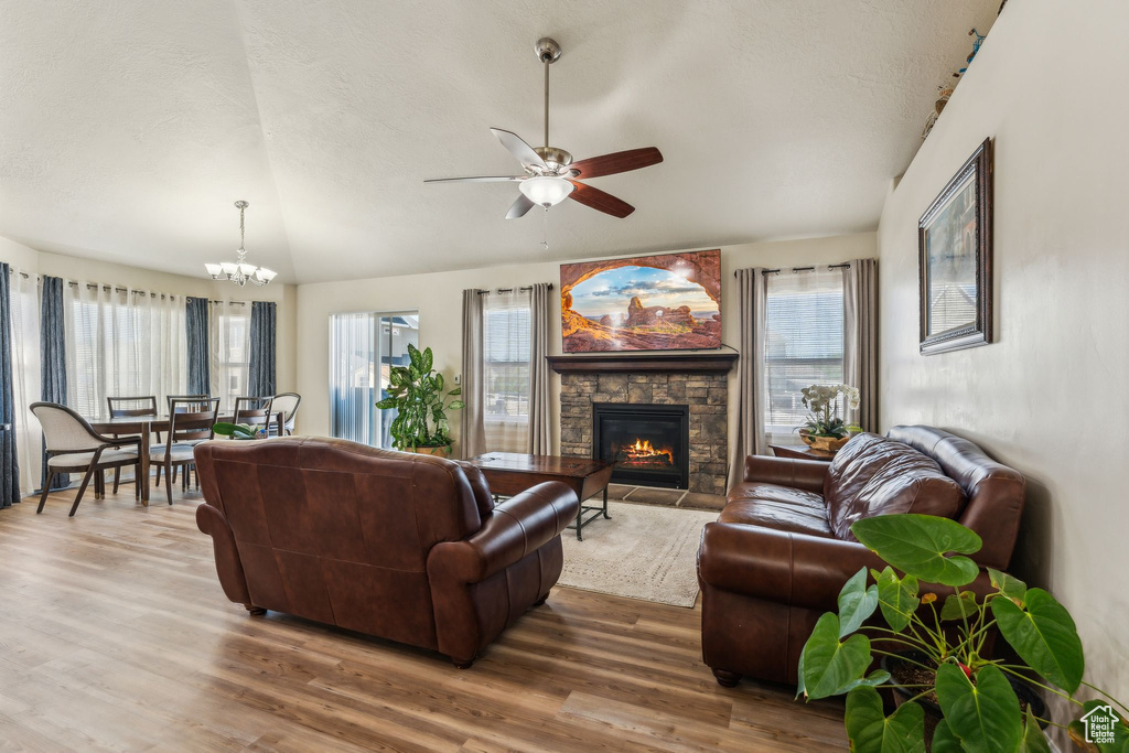 Living room featuring wood finished floors, a ceiling fan, a fireplace, a chandelier, and a textured ceiling