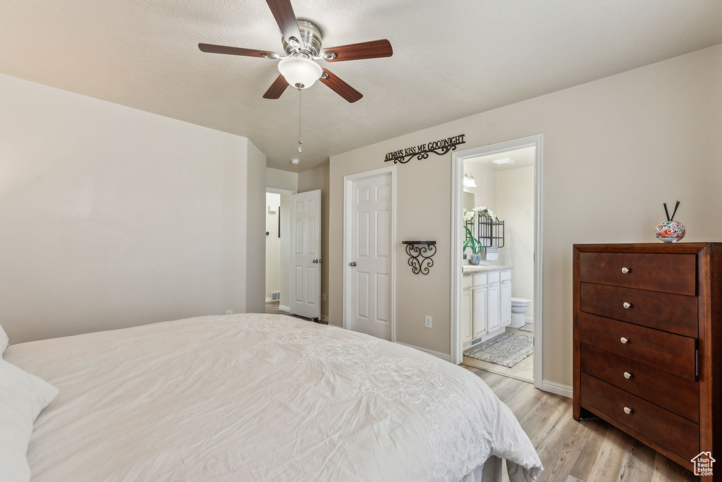 Bedroom with light wood-type flooring, ensuite bathroom, baseboards, and a ceiling fan