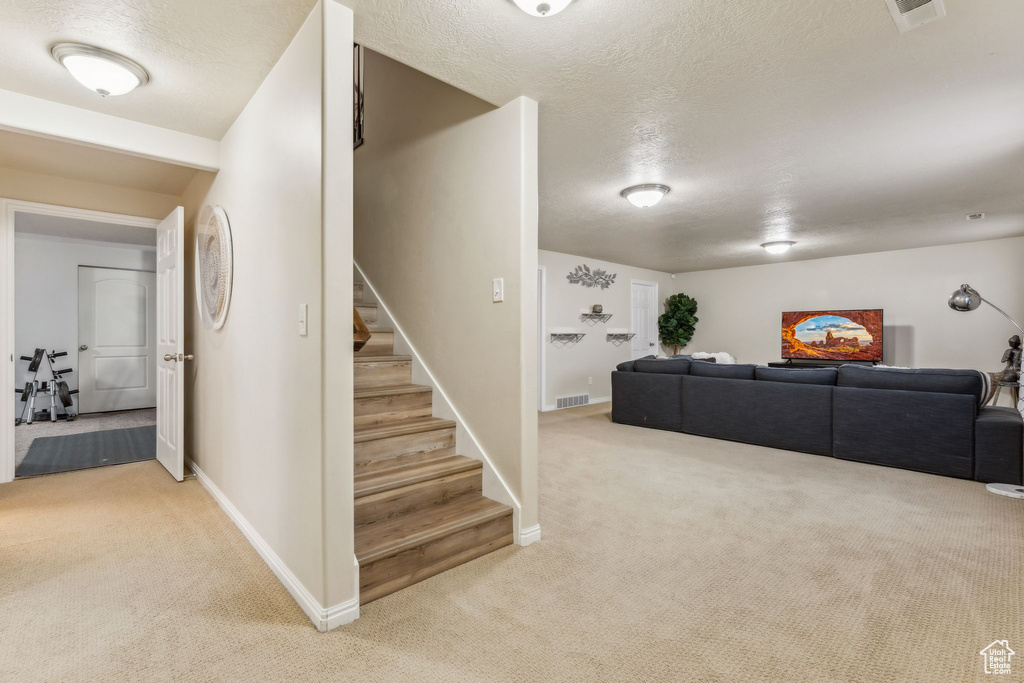 Living area featuring light colored carpet, a textured ceiling, stairs, and baseboards